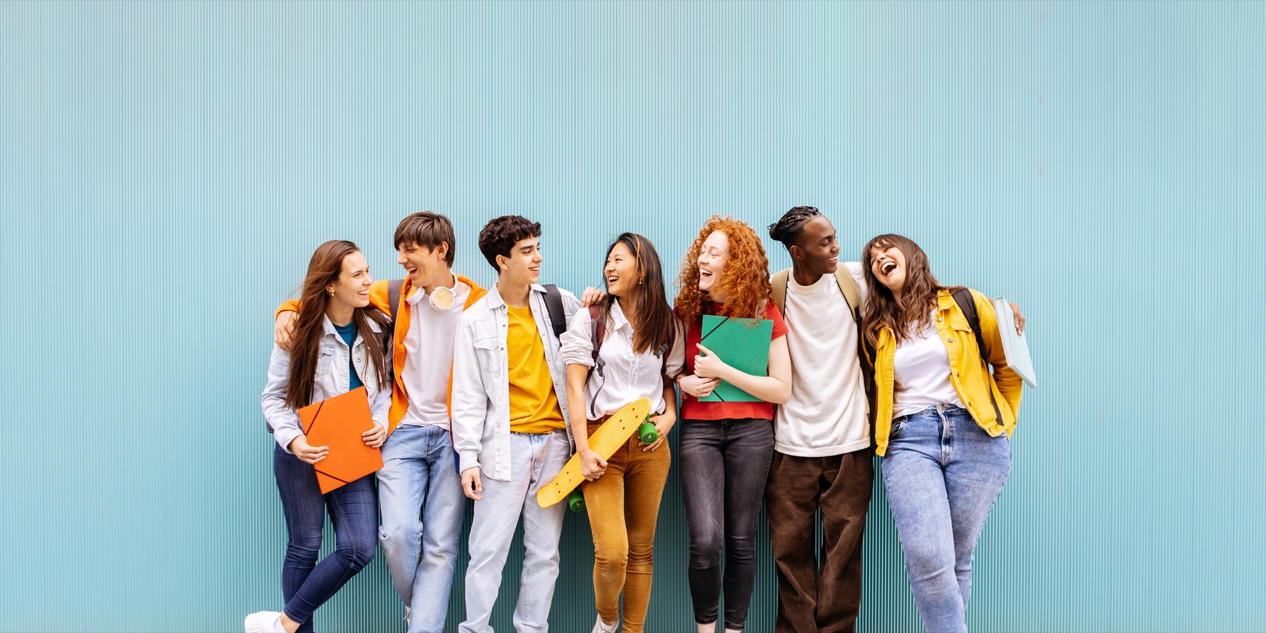 Gruppe lachender Schülerinnen und Schüler vor einer hellblauen Wand