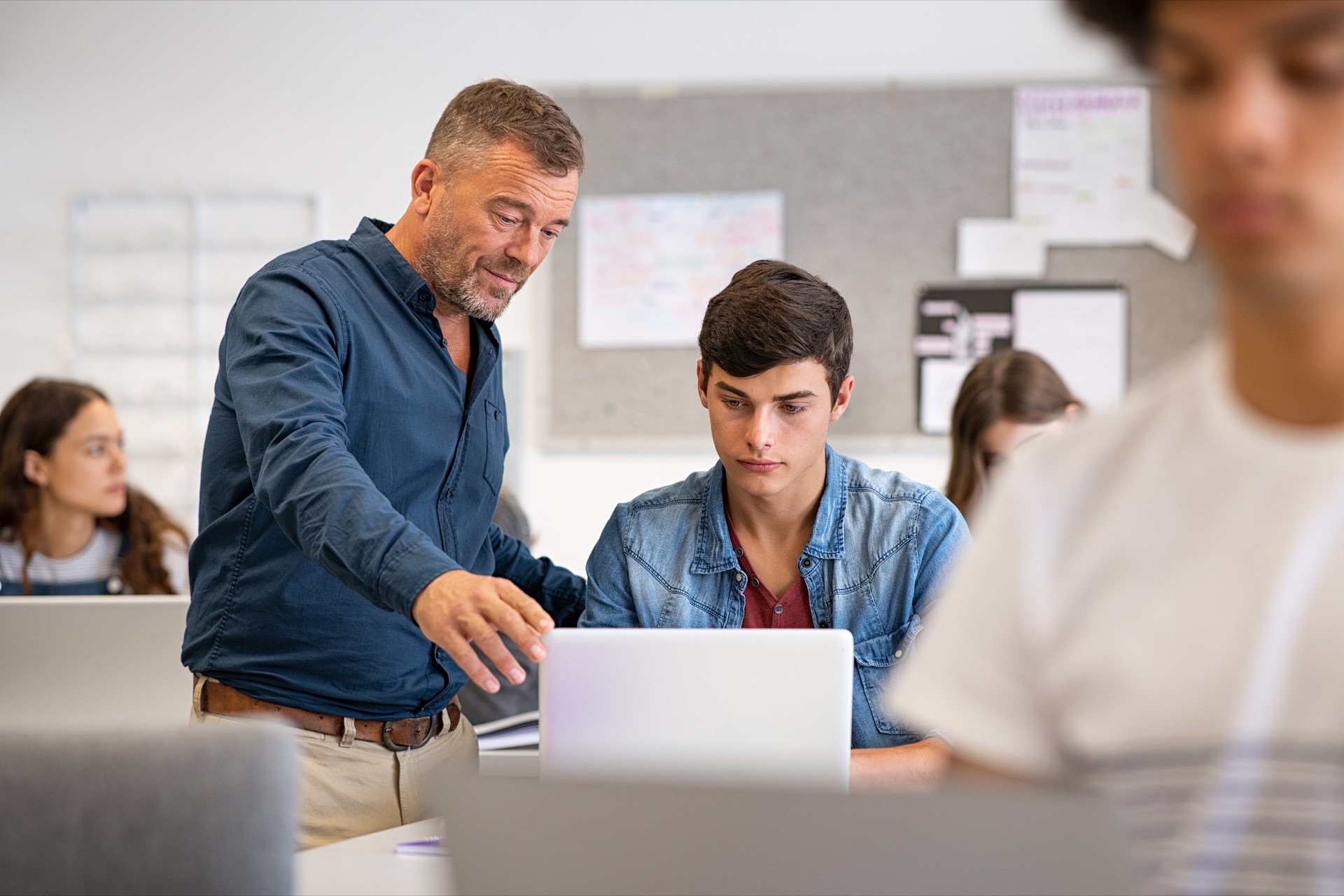 Lehrer unterstützt Schüler am Laptop
